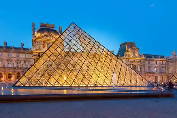 consulente di viaggio La Piramide del Louvre illuminata di sera con il palazzo storico del museo sullo sfondo.