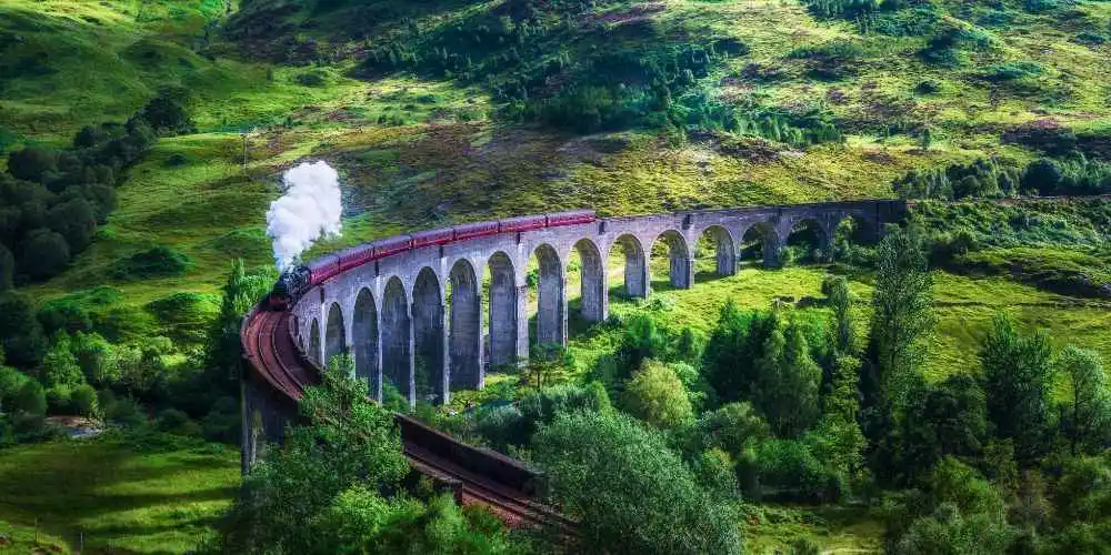Treno a vapore attraversa un viadotto in un paesaggio verde durante una vacanza in treno